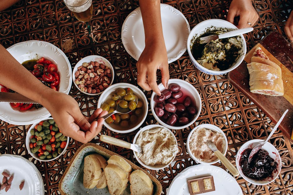 Overhead view of a rustic Mediterranean meal setup with diverse dishes and hands reaching.