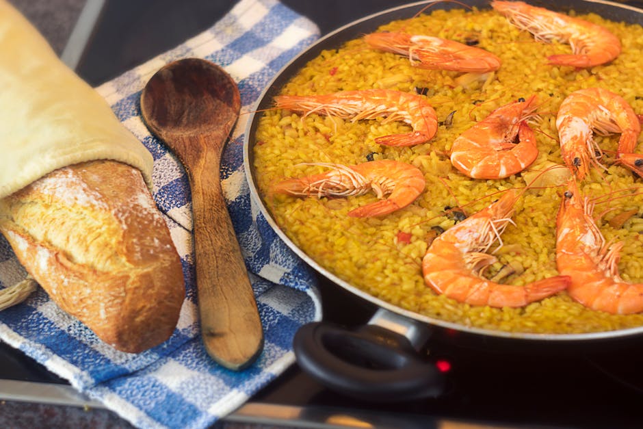 A pan of vibrant seafood paella with shrimp served next to a fresh baguette and a wooden spoon.